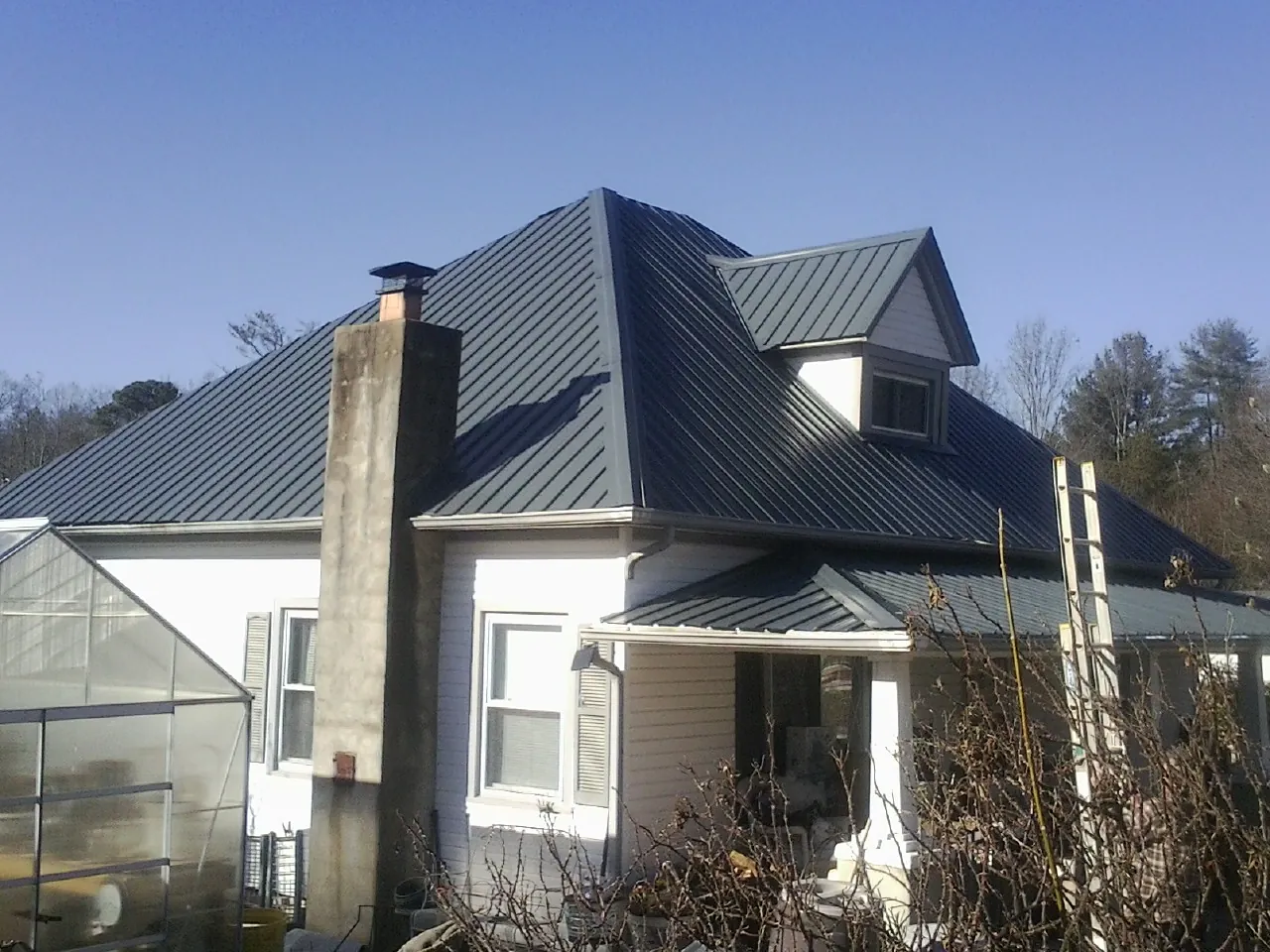 Dark blue standing seam metal roof on a white farmhouse with dormer — Slate & Tile Roof Repair by Roofing Brothers in Maple Mount