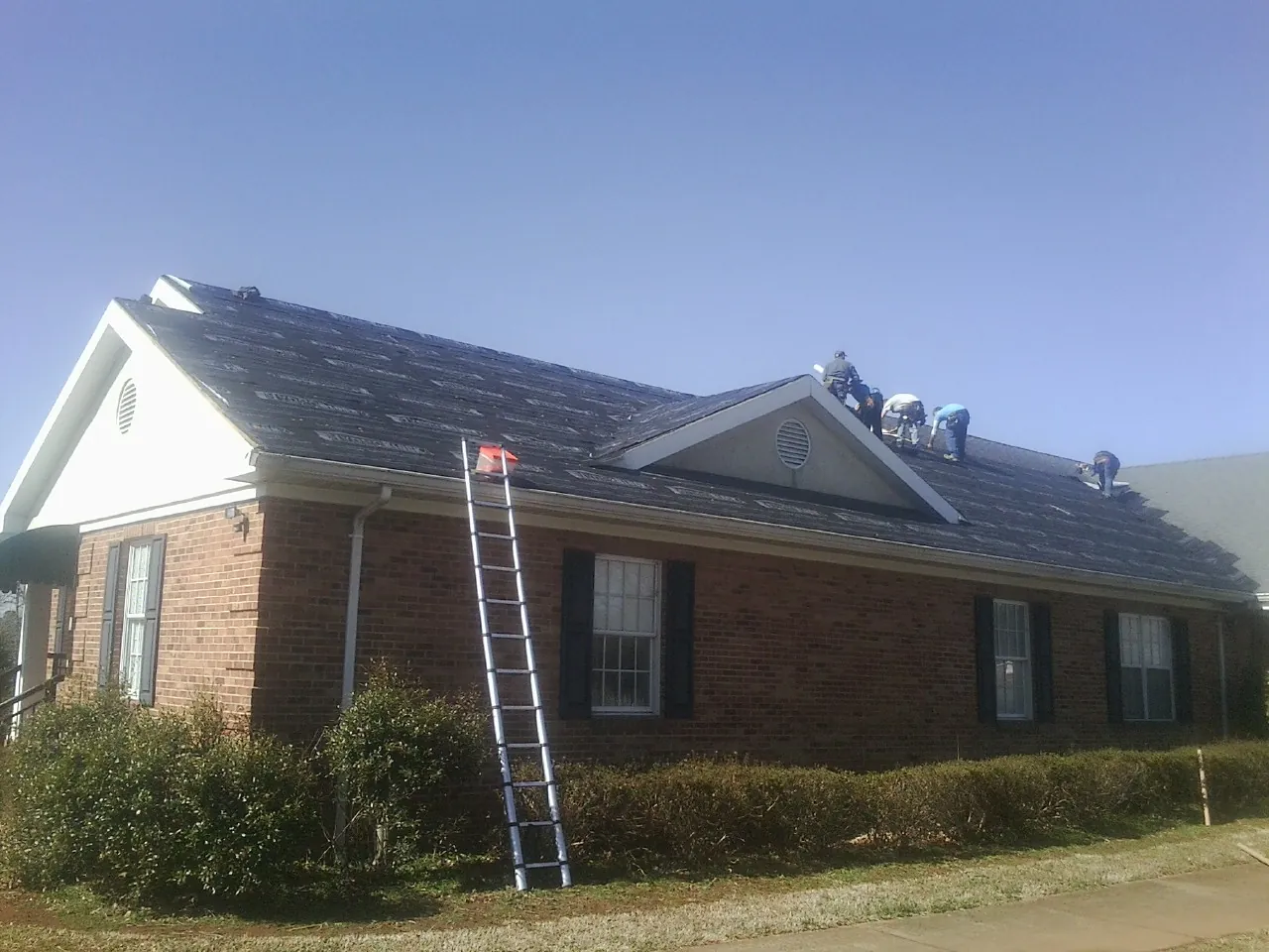 Crew tearing shingles off a brick ranch roof with a ladder set — Metal Roof Repair work by our crew in Maple Mount