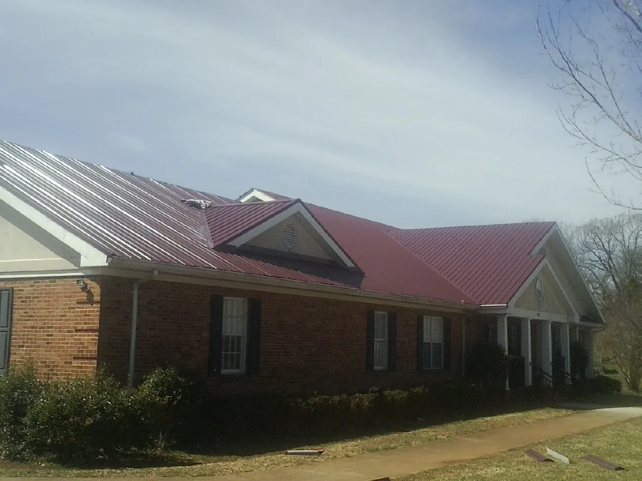 Red metal roof with gabled entries on a long brick building, from a Hail Damage Roof Repair job in Maple Mount