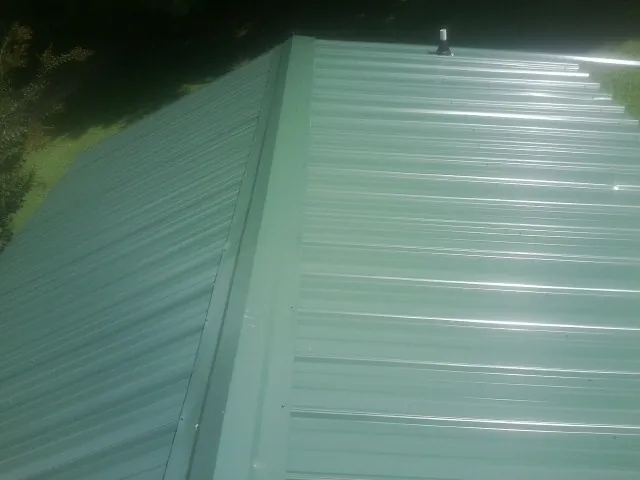 New green metal panels meeting at the ridge of a roof — Flat Roof Repair work by our crew in Maple Mount