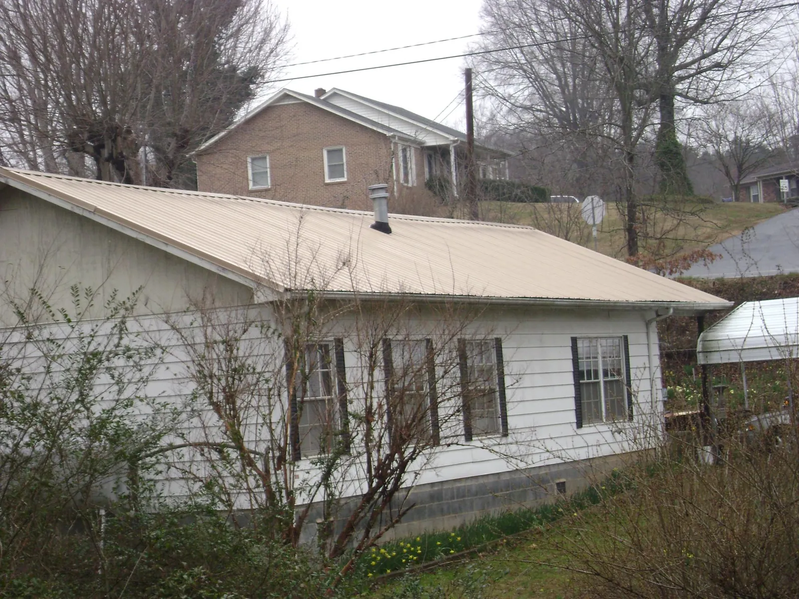 Tan metal roof on a white sided house set into a hillside — Commercial Roofing by Roofing Brothers in Maple Mount